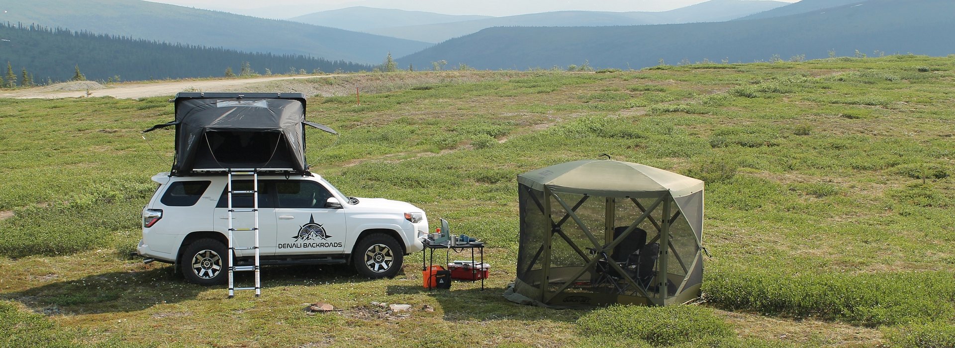 Denali Backroads Overlander vehicle with rooftop tent and gazebo shelter set up with mountain views.