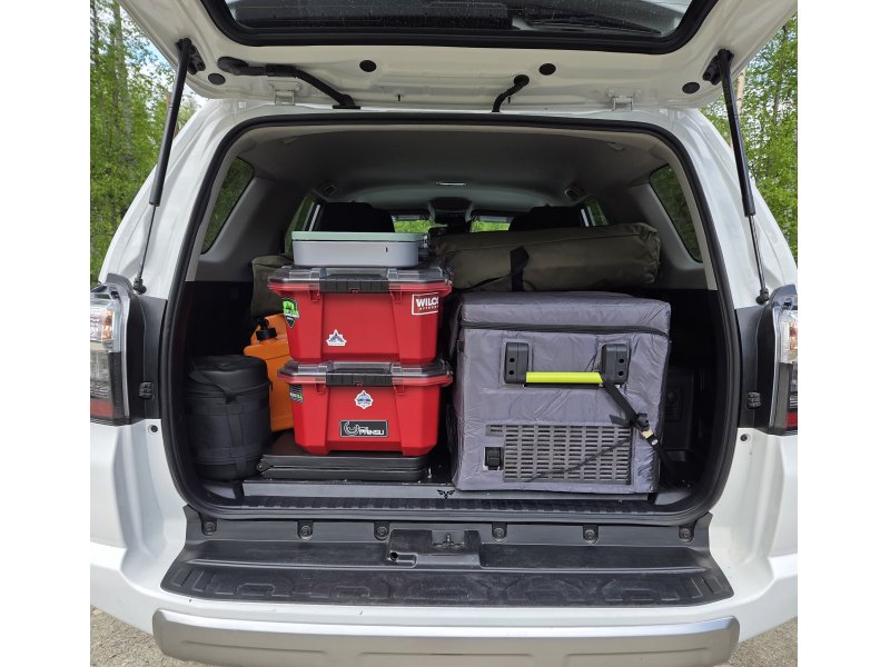 Organized rear cargo area of a Denali Backroads Overlander vehicle showing camp kitchen bins, refrigerator/freezer, cooking gear and fully equipped camping supplies ready for an Alaska adventure.