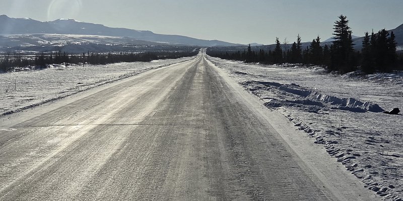 Snow-covered Alaska highway stretching into the distance representing unlimited mileage and freedom to explore remote roads.