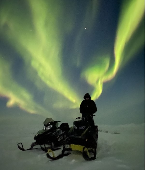 A Snow machine and Man on a lake with the Northern Lights above them
