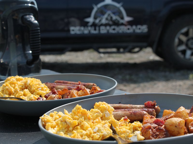 Outdoor Overlanding camp breakfast with eggs, sausage and potatoes in front of Denali Backroads adventure vehicle