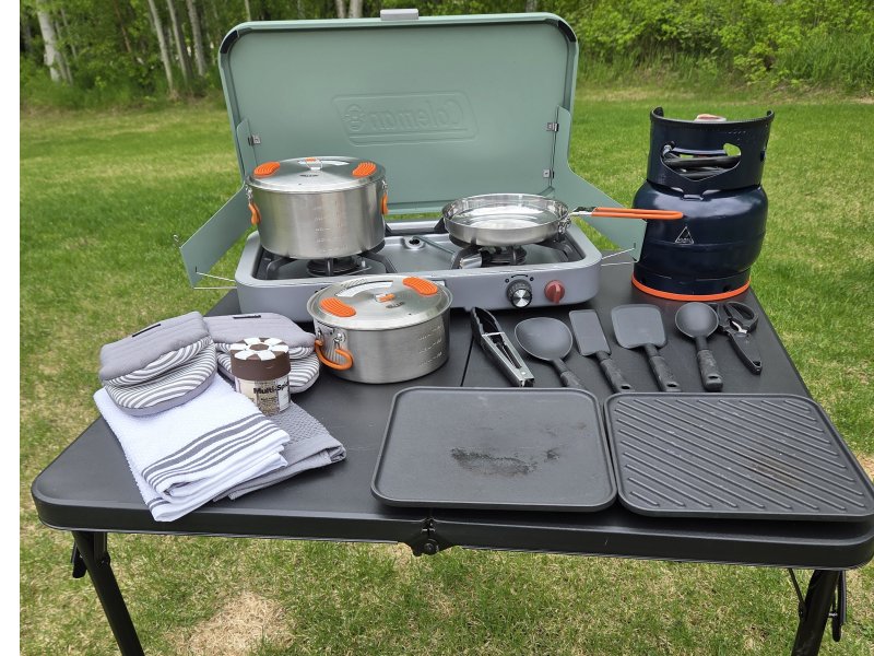 Overlanding camp kitchen with propane stove, pots, utensils and outdoor cooking gear on a folding table