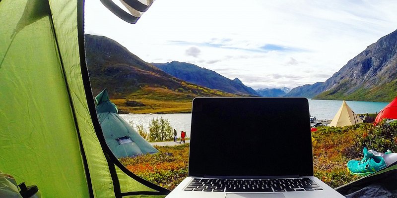 Laptop inside a camping tent overlooking a remote Alaskan lake with Starlink internet connectivity in the wilderness.