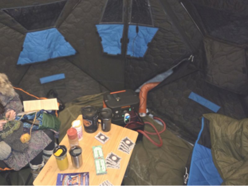 Interior of an insulated tent with table, heated power system, chairs and gear designed for comfortable Northern Lights viewing in Alaska.
